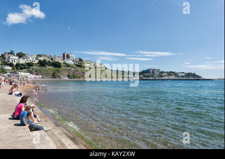 Eine Familie im Urlaub in Torre Abbey Sands, Torquay, Devon sitzt an der Promenade und bewundert den Strand und den Blick auf die Tor Bay an einem sonnigen Sommertag. Stockfoto