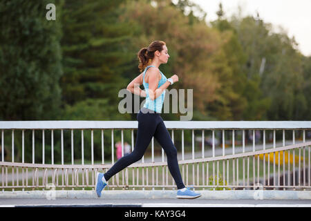Junge lächelnde sportliche Frau, die auf der Brücke am Morgen. Fitness Mädchen Jogging in der Stadt Stockfoto