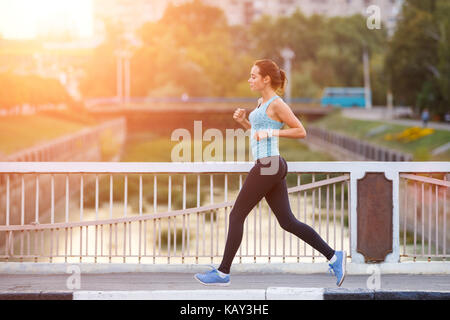 Junge lächelnde sportliche Frau, die auf der Brücke am Morgen. Fitness Mädchen Jogging in der Stadt. gesunder Lebensstil Hintergrund mit Kopie Raum Stockfoto