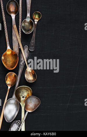 Hintergrund mit alten Silber und Gold verschiedene Löffel auf der Not schwarzen Holztisch verstreut Stockfoto