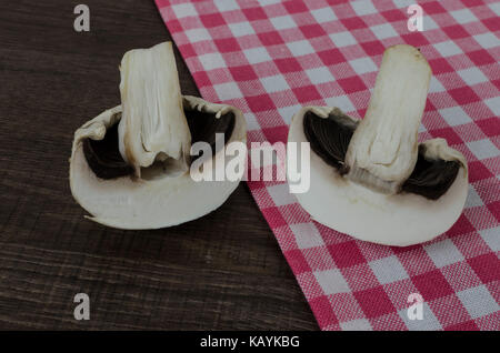 Einen einzigen Pilz in der Hälfte auf einen hölzernen Tisch eine rot-weiß-karierten Küchenhandtuch Stockfoto