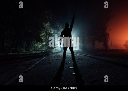 Silhouette eines Mannes mit einem erhobenen Hand in einem Park in den Strahlen des Lichts in einem Herbst neblige Nacht Stockfoto