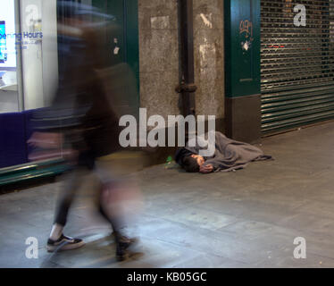 Der junge Obdachlose aus Glasgow sieht tot aus, während er bewusstlos auf dem Boden schläft, während Fremde vorbeigehen Stockfoto