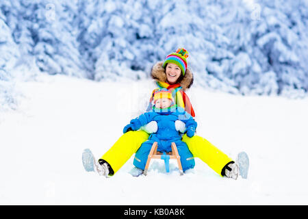 Mutter und Kind auf Schlitten fahren. Kind und Mutter rodeln. Kleinkind Kind Reiten Rodeln. Kinder spielen draußen im Schnee. Kinder Schlitten in Snowy Park. Outdoor wi Stockfoto