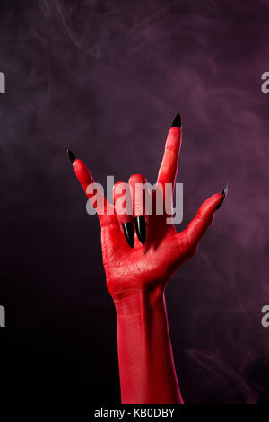 Red Devil hand mit schwarzen scharfe Nägel, studio Schuß auf smoky Hintergrund Stockfoto