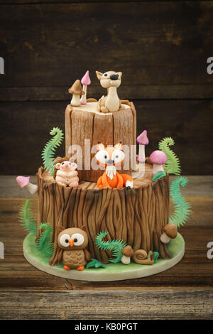 Verzauberten Wald Wald themed Fondant Kuchen mit einem Igel, Rehe, Eule, Fox, Schnecke, Baumstamm, Farne, Pilze und Blätter auf Holz- Hintergrund Stockfoto