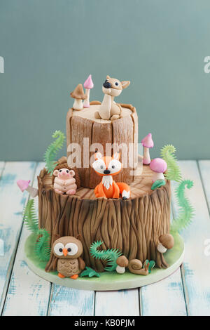 Verzauberten Wald Wald themed Fondant Kuchen mit einem Igel, Rehe, Eule, Fox, Schnecke, Baumstamm, Farne, Pilze und Blätter auf Holz- Hintergrund Stockfoto