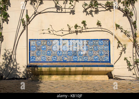 Sitzbank mit Blau handgefertigte spanische Fliesen mit einer Mauer im Hintergrund mit einer Kletterpflanze abgedeckt eingerichtet Stockfoto