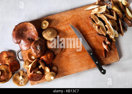 Ganze und schneiden Pilze auf einem Schneidebrett. Prozess der Schneiden und Kochen auf einem grauen Stein Tabelle Stockfoto