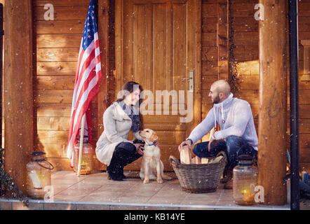 Lächelndes Paar mit Hund Vorbereitung Brennholz für Mountain House Stockfoto