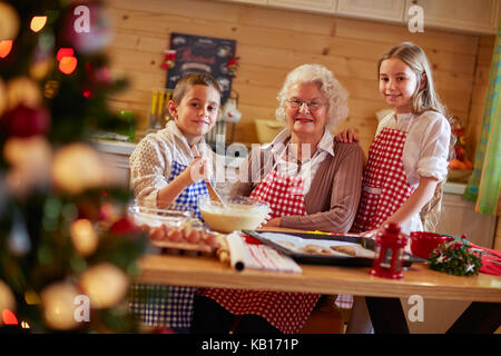 Lächelnde Kinder Vorbereitung xmas Cookies mit Großmutter zu Hause Stockfoto