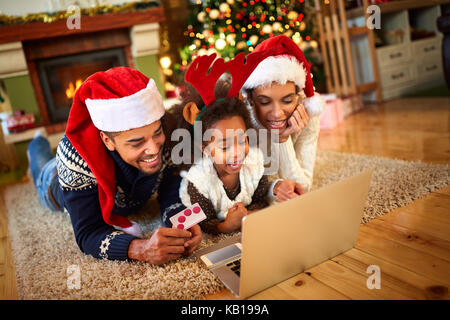 Lächelnd Familie liegen auf dem Boden vor dem Weihnachtsbaum und Laptop Stockfoto