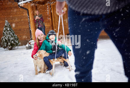 Kinder auf Schlitten im Winter Tag mit Hund auf Schnee - Familienurlaub Stockfoto