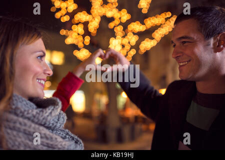 Happy freudiges Paar auf der Weihnachtszeit auf der Straße mit Herz anmelden, indem sie ihre Hände Stockfoto