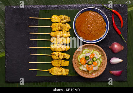 Schwein satay Spieß mit Erdnuss-sauce dekoriert mit Gurken, Zwiebel, Chili Sauce auf Banana Leaf. Stockfoto