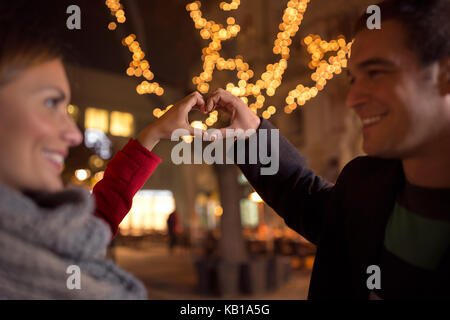 Lachen macht glücklich verliebte Herzen Form, indem sie ihre Hände mit Weihnachten Licht im Hintergrund Stockfoto