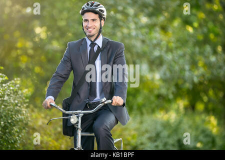 Positive junger Mann in Anzug und Fahrrad Helm mit dem Fahrrad zur Arbeit Stockfoto