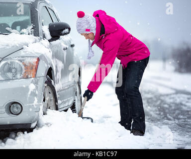 Frau schaufeln und Schneeräumung von ihrem Auto im Schnee stecken Stockfoto