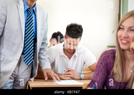 Lehrer Prüfung der studentischen Arbeiten in einem Klassenzimmer Stockfoto