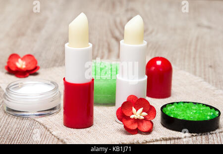 Kosmetik für die Lippe Hautpflege: Close-up von Meersalz, natürlicher Honig Peeling mit ätherischen Ölen, lip Cream und Balsame mit Blumen auf schäbige Holz- Oberfläche Stockfoto