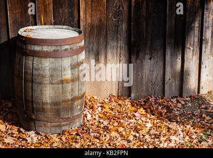 Rustikale vintage Holzfass durch Scheune Wand stehend auf trockene Blätter im Herbst am Boden. Stockfoto