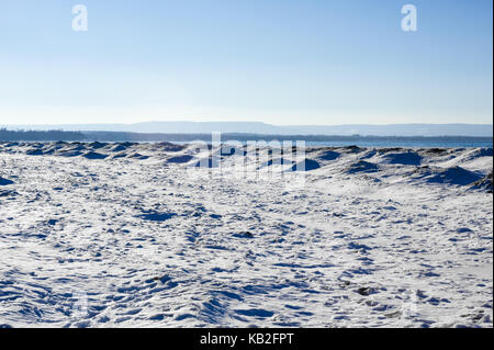 Gefrorenes Eis, Schnee und Sanddünen am Strand im Winter am See unter dem klaren, blauen Himmel mit Hügeln in der Entfernung, in der Nähe der Georgian Bay, Ontario, Kanada. Stockfoto