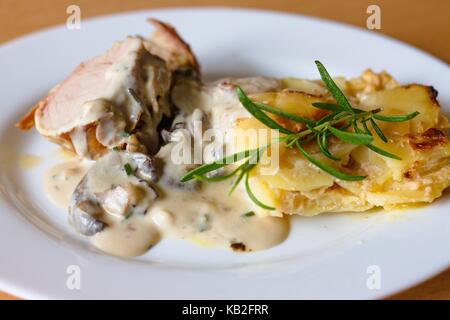 Schweinefilet im Speckmantel gebraten Koteletts mit Pilzsauce und gebratenen Kartoffeln. Selektiver Fokus auf gerösteten Kartoffeln. Stockfoto