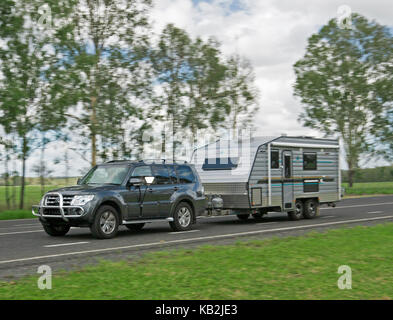 Dunkelgrau Allradantrieb Fahrzeug Faltcaravan entlang Bitumen Straße gegen den Hintergrund der Bäume, Ackerland und blauer Himmel in Australien Stockfoto