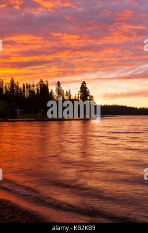 Friedlichen und farbenfrohen Red Sky sunrise im Diamond See mit Wellen plätschern am Ufer und Kiefer Silhouetten auf dem fernen Ufer, Oregon, USA. Stockfoto