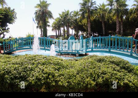 Eine hölzerne Brücke über den Pool mit Springbrunnen im Park des 100. Jahrestages von Atatürk (Alanya, Türkei). Stockfoto