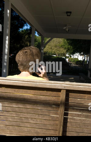 Kaukasisches Senioren-Paar (60-70) sitzt im Schaukel, während es auf dem Handy spricht. USA Stockfoto