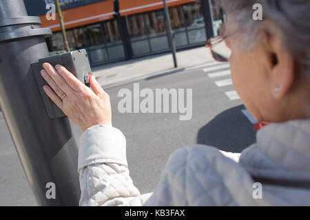 Alte Dame durch Drücken der Taste an der Ampel am Zebrastreifen Stockfoto