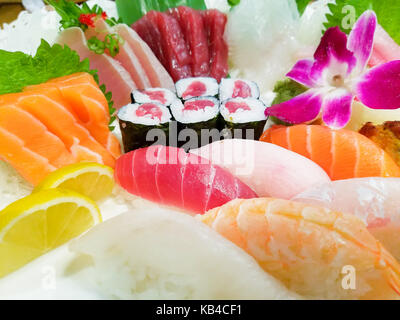 Close-up verschiedener Sushi, serviert auf einem Teller mit einer Orchidee. Stockfoto