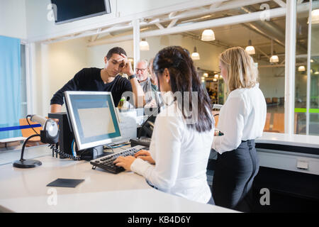 Müde männlichen Fahrgast warten am Check-in, während die weiblichen mit computer Personal im Flughafen Stockfoto