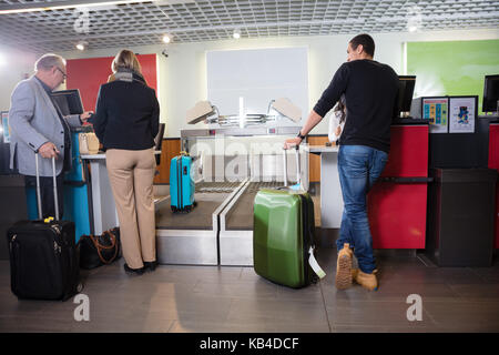 Männliche und weibliche Passagiere mit Gepäck am Flughafen Check-in-Schalter Stockfoto