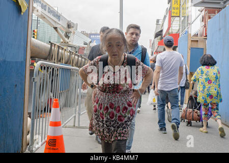 Eine ältere chinesische Frau hinunter Hauptstraße mit einem ernsten Ausdruck in Chinatown, Flushing, Queens, New York City. Stockfoto
