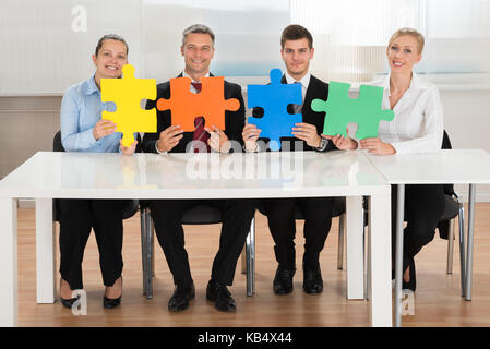 Team von Geschäftsleuten Holding Vier mehrfarbige Puzzles am Schreibtisch Stockfoto