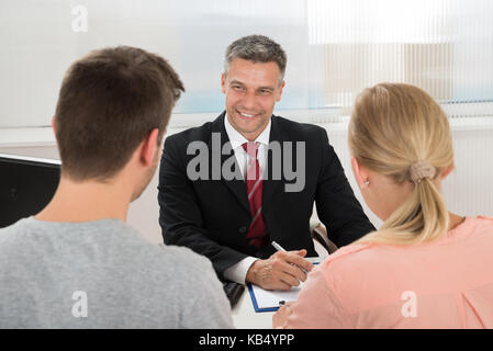 Reifen glücklich Immobilienmakler im Gespräch mit jungen Paares im Büro Stockfoto