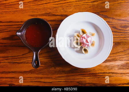 Die Zusammensetzung der Platte mit Knödel mit rosa Sauerrahm und borsch in der Pfanne abgedeckt. Stockfoto