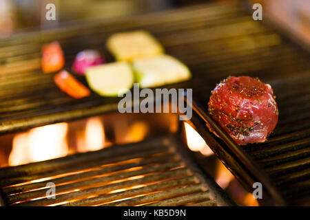 Der Blick auf den Gewürzten rohes Fleisch auf dem brazier platziert Mit dem Verbrennen von Holz im Restaurant Küche. Stockfoto