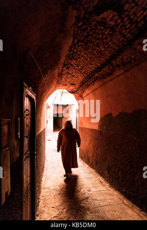 Lokaler Mann in traditionellen djellaba gekleidet zu Fuß durch Torbogen in einer Straße in der Kasbah, Marrakesch, Marokko, Nordafrika Stockfoto