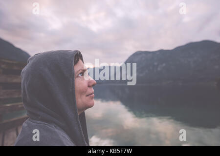 Nostalgische Portrait von einsam melancholisch erwachsene Frau mit hoffnungsvollem Blick in Richtung Himmel stand am Ufer des Sees in Misty bewölkten Morgen, retro bis Stockfoto