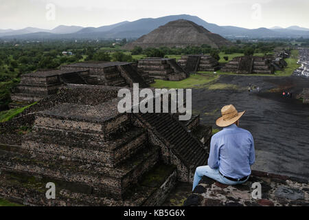 Ein Mann sitzt auf einem Felsvorsprung mit Blick auf Teotihuacán, eine alte mesoamerikanische Stadt in einem Subtal des Tals von Mexiko. Stockfoto