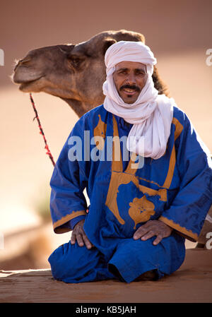 Berber Mann mit Kamel, Ruhen im Erg Chebbi Sand Meer, Teil der Sahara Wüste in der Nähe von Fes, Marokko, Nordafrika Stockfoto