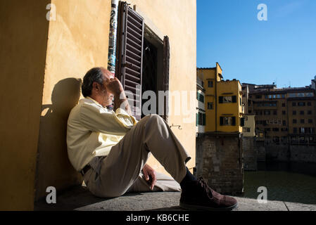 Ein Mann sitzt nachdenklich auf den Arno mit der Ponte Vecchio Brücke auf der Rückseite. Florenz, Italien Stockfoto