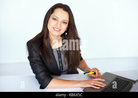 Portrait von schönen Jungen lächelnd brunette business Frau, die an einem Notebook arbeitet im Büro Stockfoto