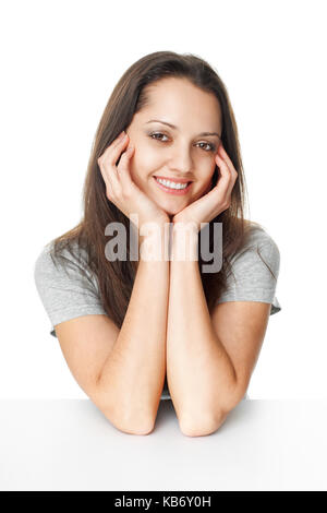 Porträt der hübsche junge brünette Frau mit den Ellenbogen auf den Tisch und das Kinn auf die Hände auf weißem Hintergrund basierend Stockfoto