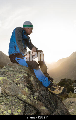 Gut aussehende junge Wanderer eine Pause auf einem Stein und genießt den Sonnenaufgang in den Schweizer Bergen Stockfoto