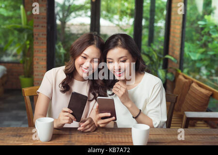 Zwei junge business Frauen am Tisch sitzen im Cafe. Mädchen zeigt ihrer Freundin Bild auf dem Bildschirm des Smartphones Stockfoto