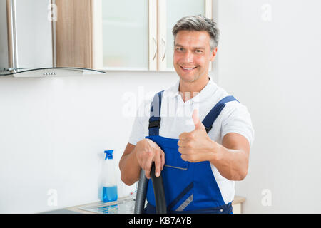 Portrait von glücklichen männlichen Hausmeister Gestik Daumen oben in der Küche Stockfoto